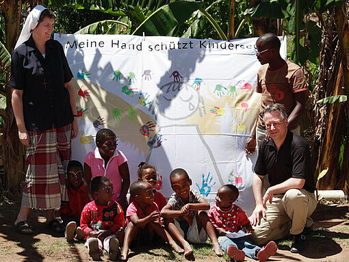 Schwester Silke Mallmann steht mit südafrikanischen Kindern vor einem Banner der Aktion Schutzengel von missio.