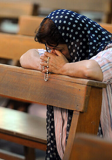 Eine chaldäische Christin kniet auf einer Bank in einem Gottesdienst in Erbil und betet.