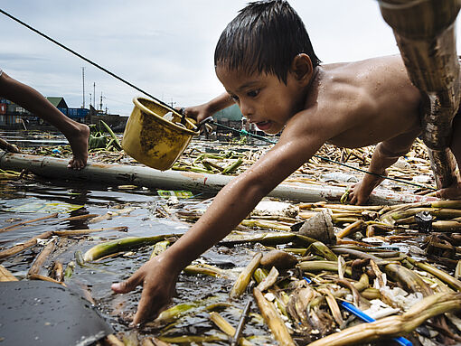Der kleine Junge sammelt Müll im Wasserslum Happyland auf den Philippinen