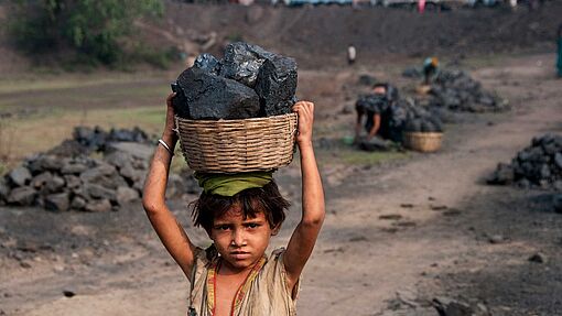 Ein kleines Mädchen trägt auf einer Kohlehalde in Jharia Kohlestücke auf seinem Kopf weg.