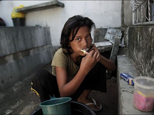 Ein Mädchen sitzt Zähne putzend auf dem Friedhof in Cebu