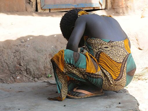 Ein afrikanisches Mädchen hockt auf dem Boden und dreht sich weg.