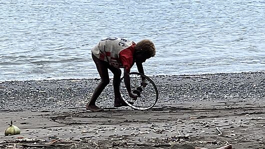 Ein Junge spielt mit Fahrradfelge am Strand von Buma.