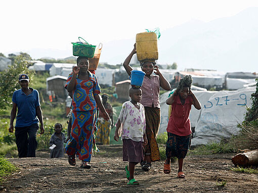 Flüchtlinge, die in einer Zeltstadt am Kivu See in der Demokratischen Republik Kongo leben, tragen Eimer und Körbe auf ihren Köpfen.