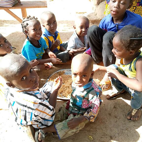 Kinder sitzen im Kreis um eine Pfanne herum und essen Reis.