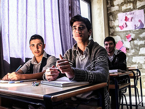 Drei syrische Jugendliche sitzen in einem Klassenraum.