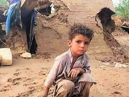 Ein Junge sitzt nach den Überschwemmungen in Pakistan vor einem zerstörten Haus
