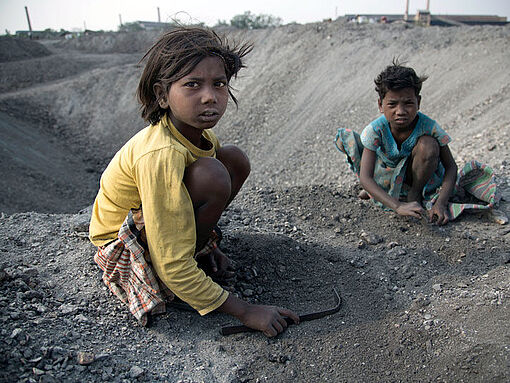 Zwei Kinder sammeln Kohle auf einer Halde.