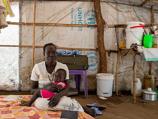 Eine junge Mutter sitzt mit ihrem Baby auf einem Bett in einem Flüchtlingscamp in Juba.
