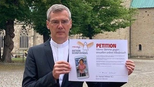 Vor dem Hildesheimer Dom hält Bischof Dr. Heiner Wilmer die unterzeichnete Petition hoch. 