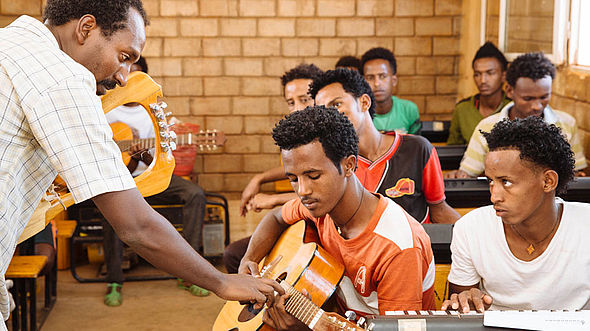 Im Flüchtlingslager können diese jungen Männer lernen, wie man Gitarre spielt. 