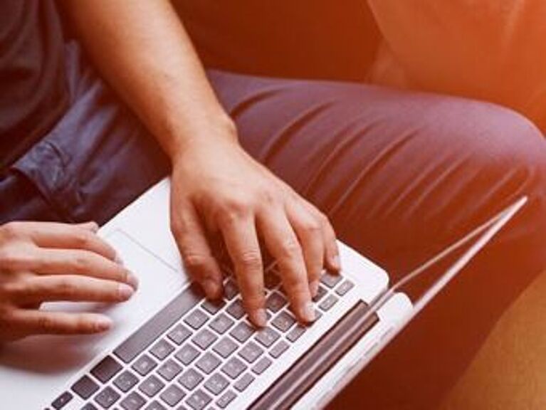 Bild von Männerhänden, die auf einer Laptoptastatur liegen.