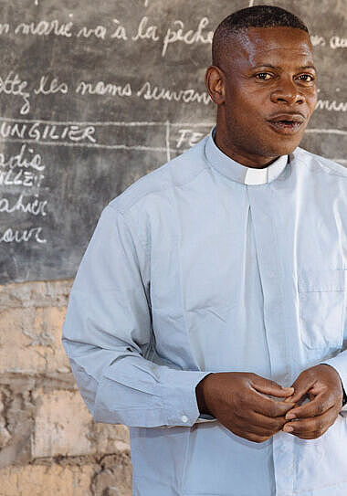 Priester Gustave steht vor einer Tafel in einer Schule in Kasongo.