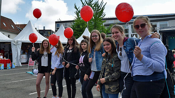 Eine Mädchengruppe steht mit den Luftballons der Aktion #dafürhalteichmeinenkopfhin auf dem Aegidiimarkt in Münster.
