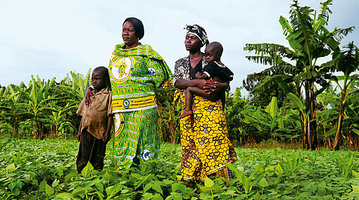 Thérèse Mema und eine Frau mit Kindern stehen auf einem Feld im Kongo.