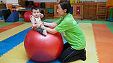 Auf dem Gymnastikball kann das Kleinkind mit Behinderung sitzen üben. 