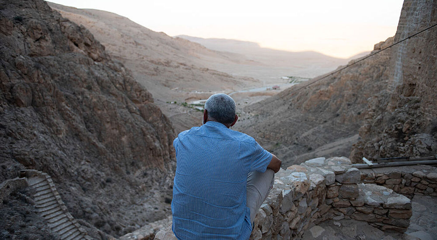 Ein Mann sitzt vor dem syrischen Kloster Mar Musa und blickt ins Tal.