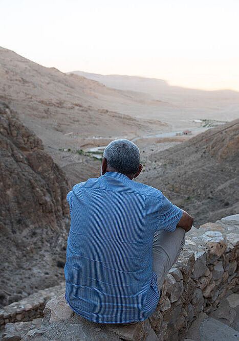 Ein Mann sitzt vor dem syrischen Kloster Mar Musa und blickt ins Tal.