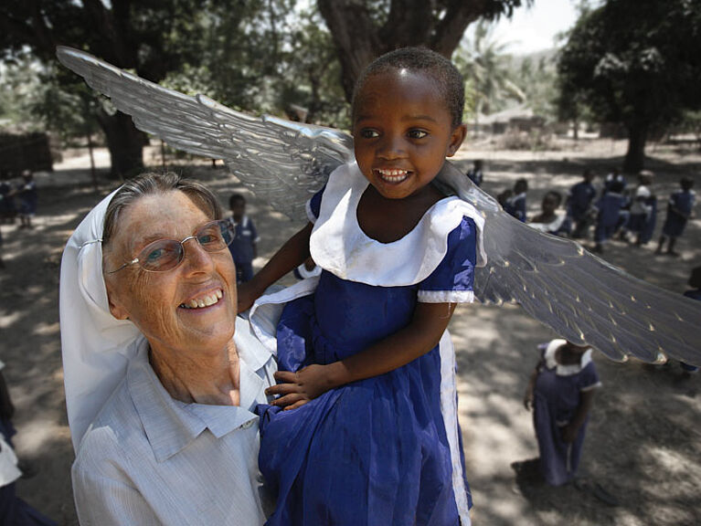 Schwester Raphaela Händler hält in einem Kindergarten in Tansania ein Mädchen mit Engelsflügeln auf dem Arm.
