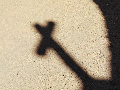 Die Sonne wirft den Schatten eines Kreuzes an eine Mauer