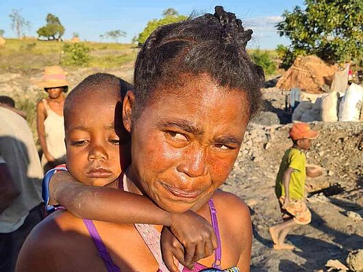 Eine Frau, in auf Madagaskar in den Minen Mica abbaut, trägt ihr kleines Kind auf dem Rücken.