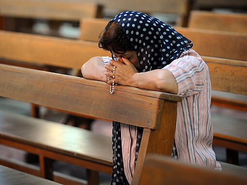 Eine chaldäische Christin kniet auf einer Bank in einem Gottesdienst in Erbil und betet.