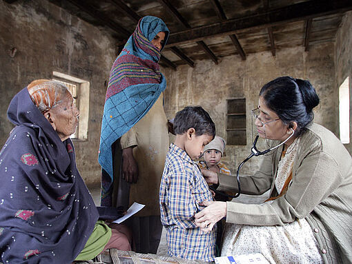 Eine Frau untersucht einen kleinen Jungen in einer ärmlichen Umgebung in Indien.