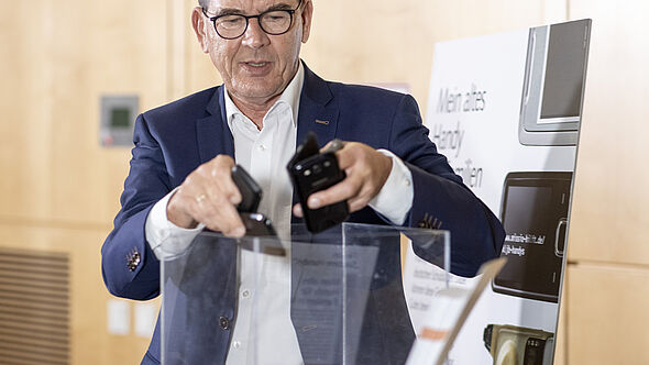 Bundesminister a.D. Gerd Müller wirft Handys in eine Spendenbox. 