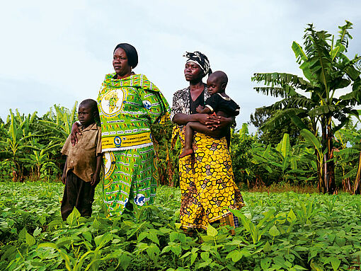 Thérèse Mema und eine Frau mit Kindern stehen auf einem Feld im Kongo.