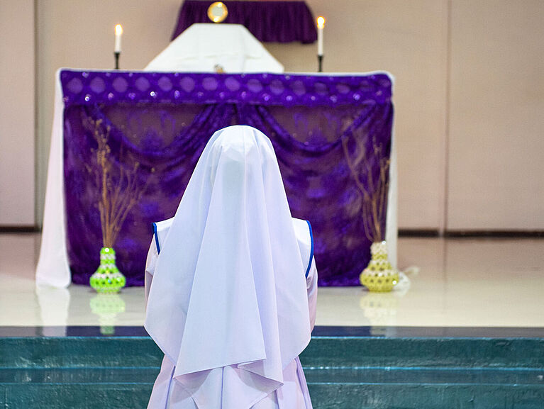 Eine Ordensfrau kniet vor dem Altar und betet