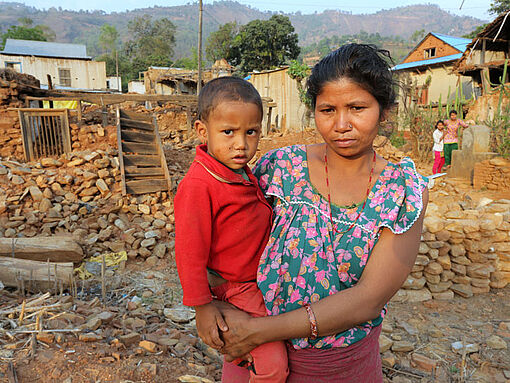 Die junge Frau Sanu Naga Danwar steht mit ihrem Kind vor ihrem vom Erdbeben zerstörten Haus. 