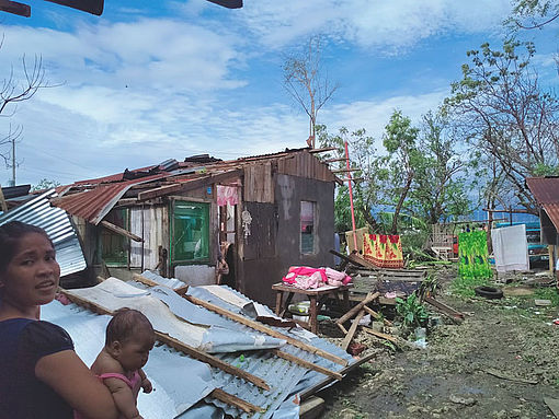 Eine Mutter steht mit ihrem Baby vor dem von Taifun Rai zerstörten Haus.
