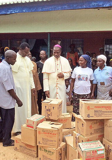 Bischof Stephen Mamza mit Dorfbewohnern vor Kartons mit Lebensmitteln.