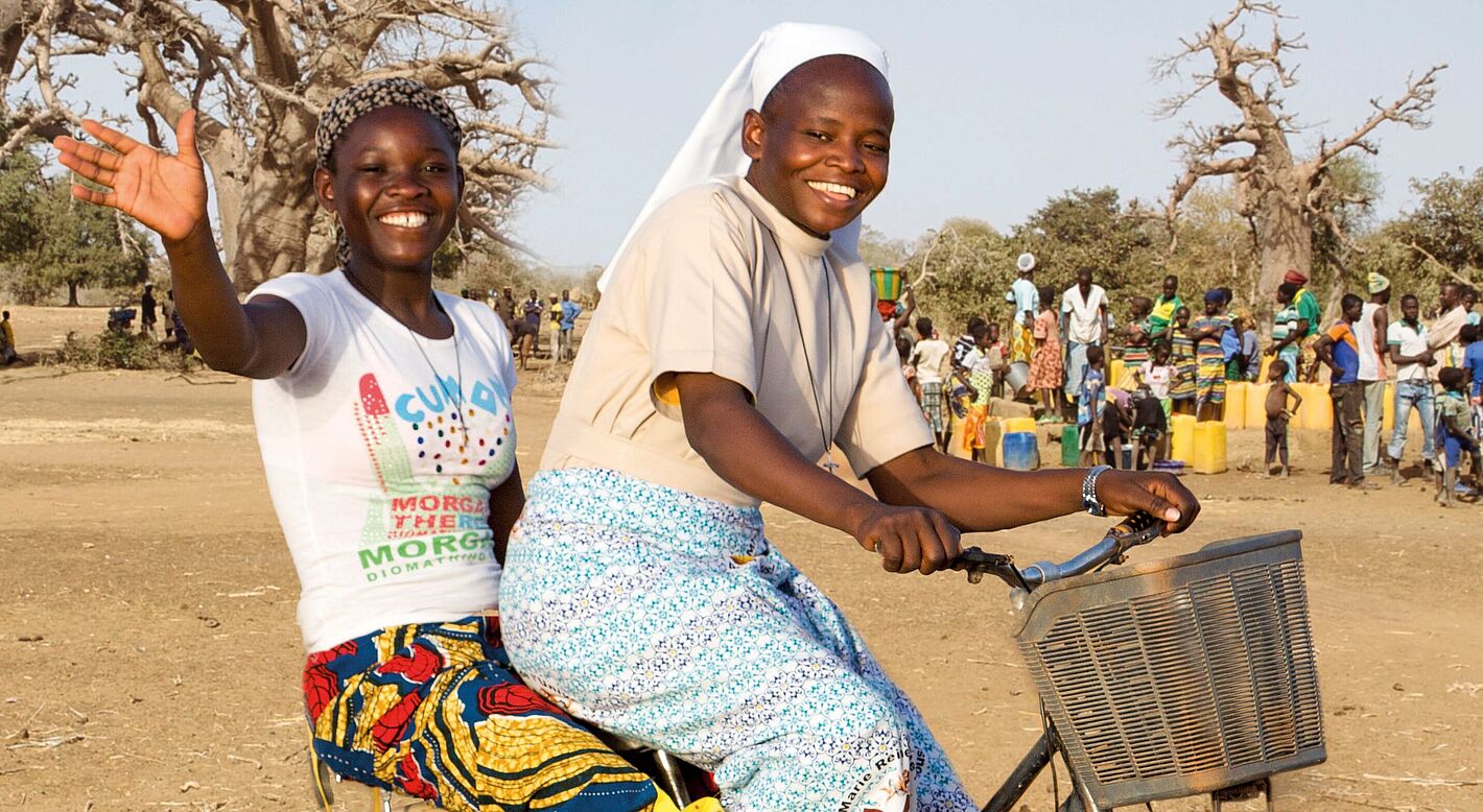Burkina Faso, eine Ordensschwester nimmt ein Mädchen auf dem Gepäckträger ihres Fahrrads mit.
