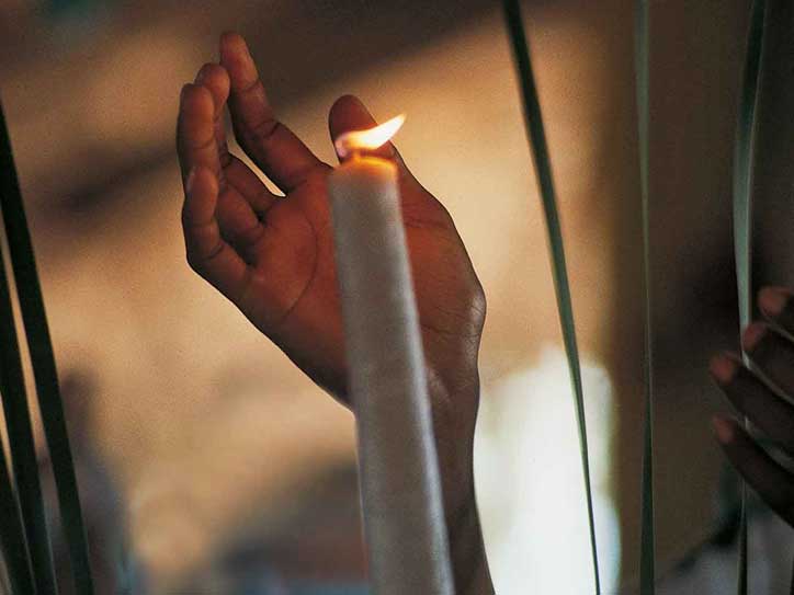 Eine Hand schützt eine brennende Kerze